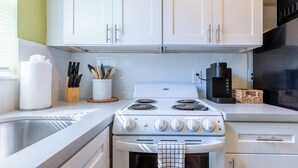Una cocina con armarios blancos, estufa, fregadero y cafetera.