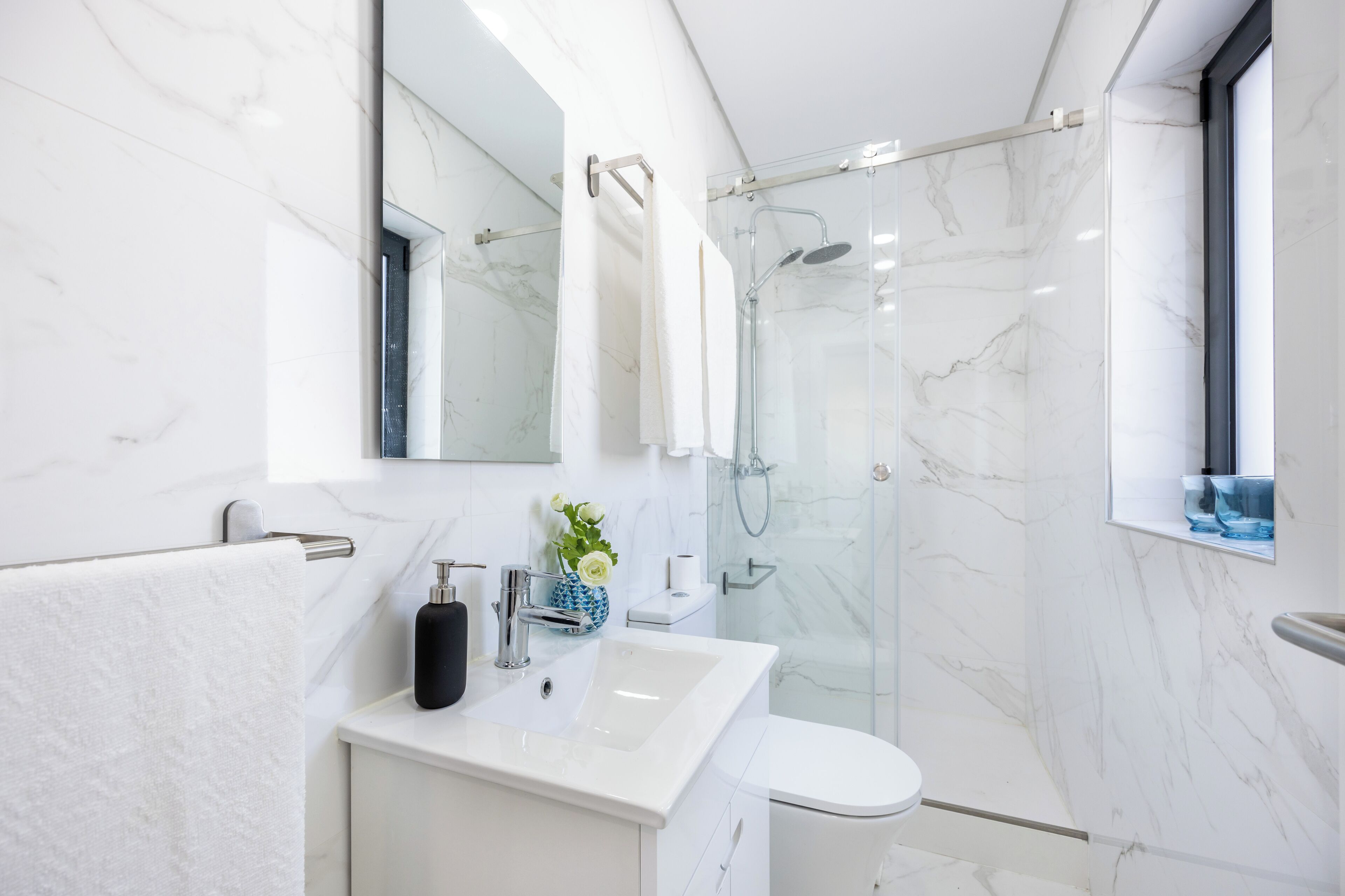Une salle de bain moderne avec un lavabo en marbre blanc, une cabine de douche en verre et un grand miroir au-dessus du lavabo.
