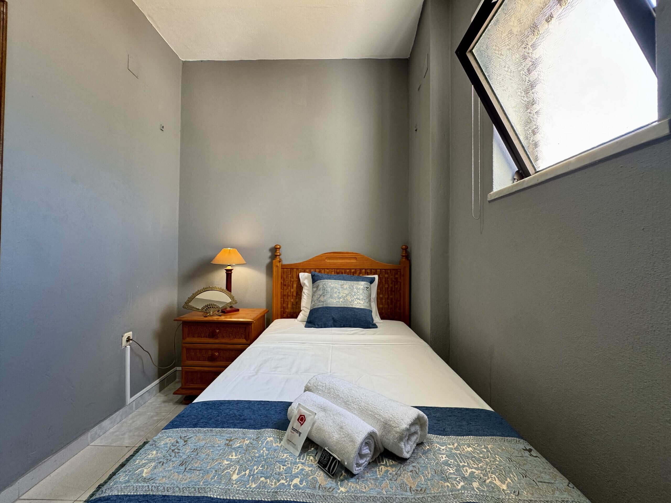 Een slaapkamer met een bed, nachtkastje, lamp, raam en een wandradiator.