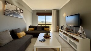 A living room with a sofa, a coffee table, a TV, and a large window with a view. - Albufeira Central 8 by Homing (Albufeira)