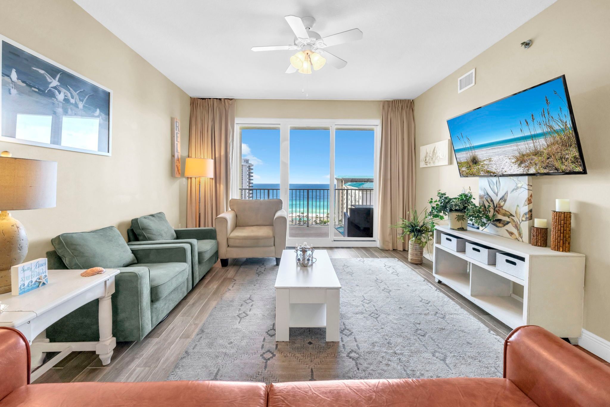 A living room with a view of the ocean, a ceiling fan, and a large window.