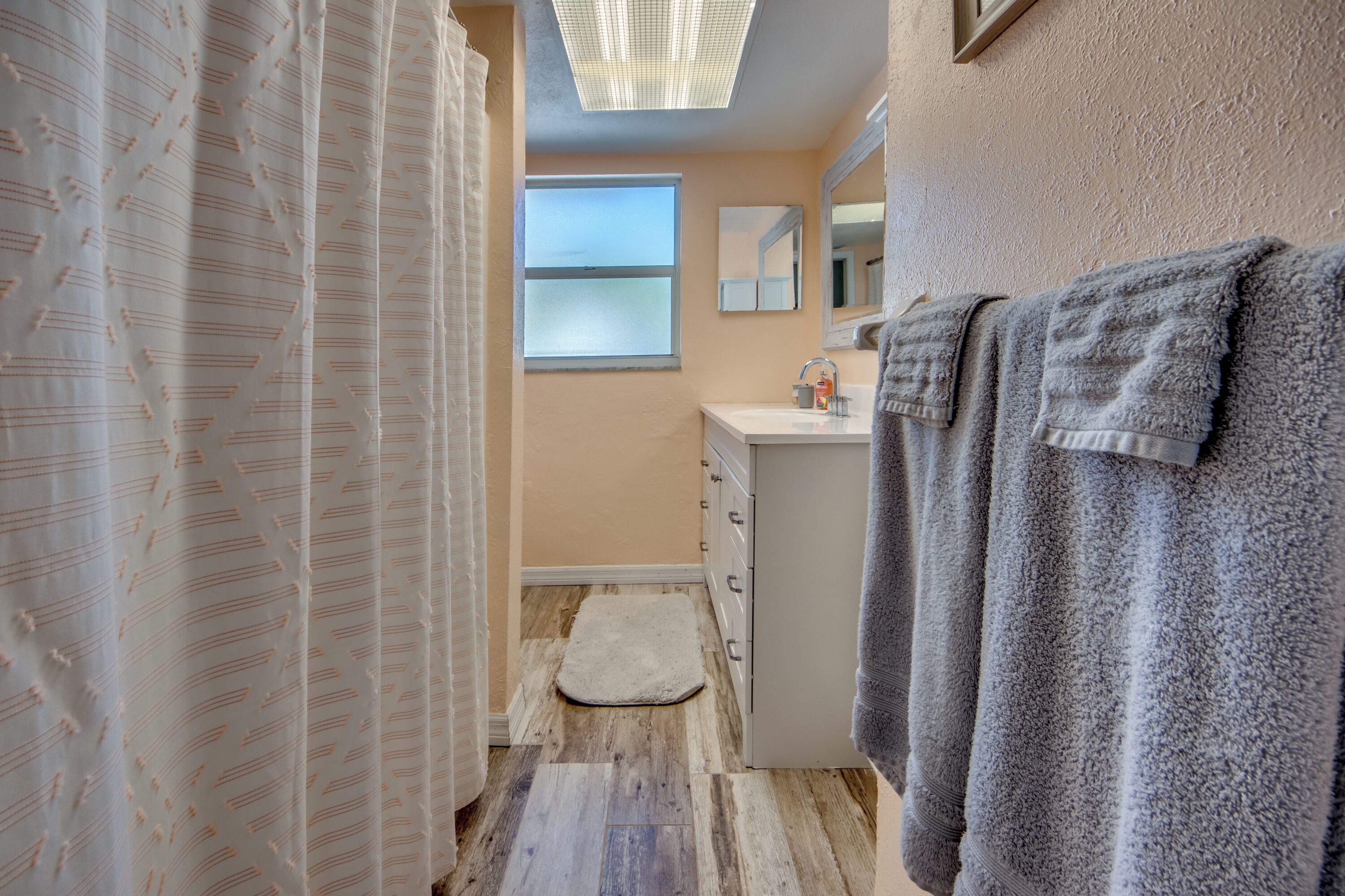 Un bagno con tenda doccia, lavandino, specchio e asciugamani.