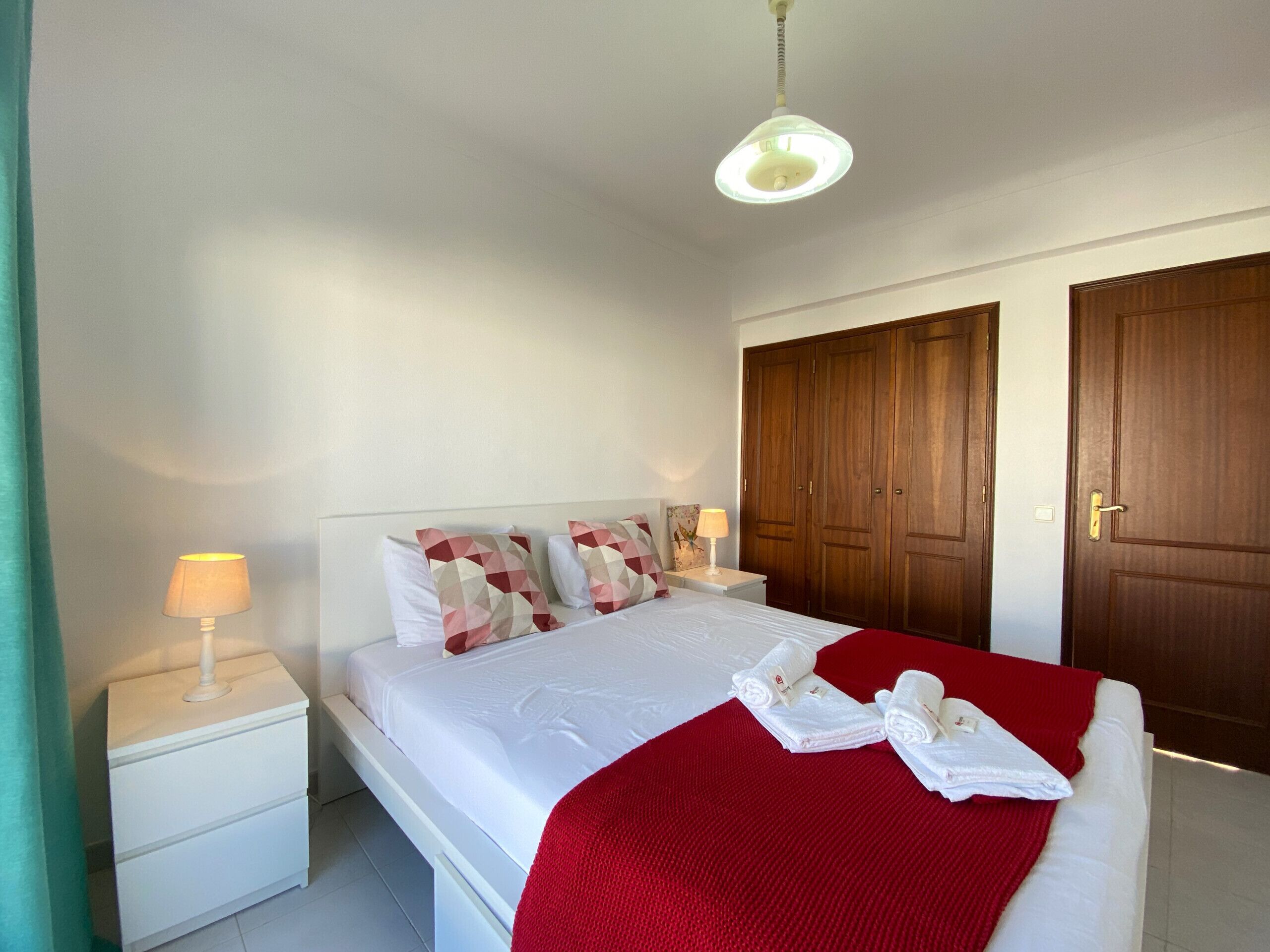 A hotel room with a bed, nightstands, a red blanket, and wooden doors.