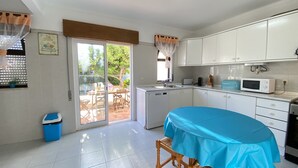 Una cocina con armarios blancos, un microondas y una mesa cubierta con mantel azul.