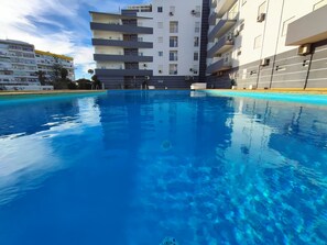 En swimmingpool med ett klart, blått vatten, omgiven av moderna byggnader med balkonger och luftkonditioneringsanläggningar.