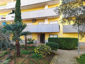 A multi-story yellow building with balconies, a garden with yellow flowers, and a cobblestone pathway. - Armação DE Pêra Ocean Terrace by Homing (Silves)