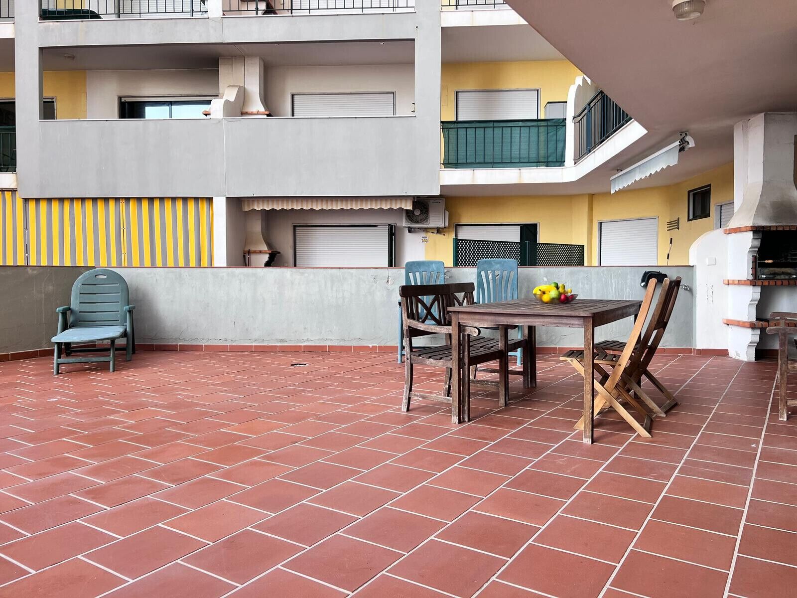 Eine Terrasse mit Tisch und Stühlen, einem Grill und einem gelben Gebäude im Hintergrund.