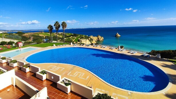 A large, curved swimming pool with a clear view of the ocean and rocky coastline in the background. - Lagos Ocean BAY With Pool by Homing (Lagos)