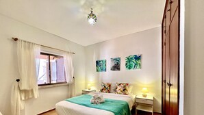 A bedroom with a bed, two bedside tables, a window with curtains, a wall-mounted lamp, and a door. - Lagos Ocean BAY With Pool by Homing (Lagos)