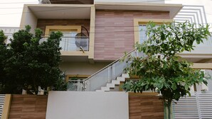 Et moderne hus med to etager, en balkon, en trappe og et træ i forgrunden.