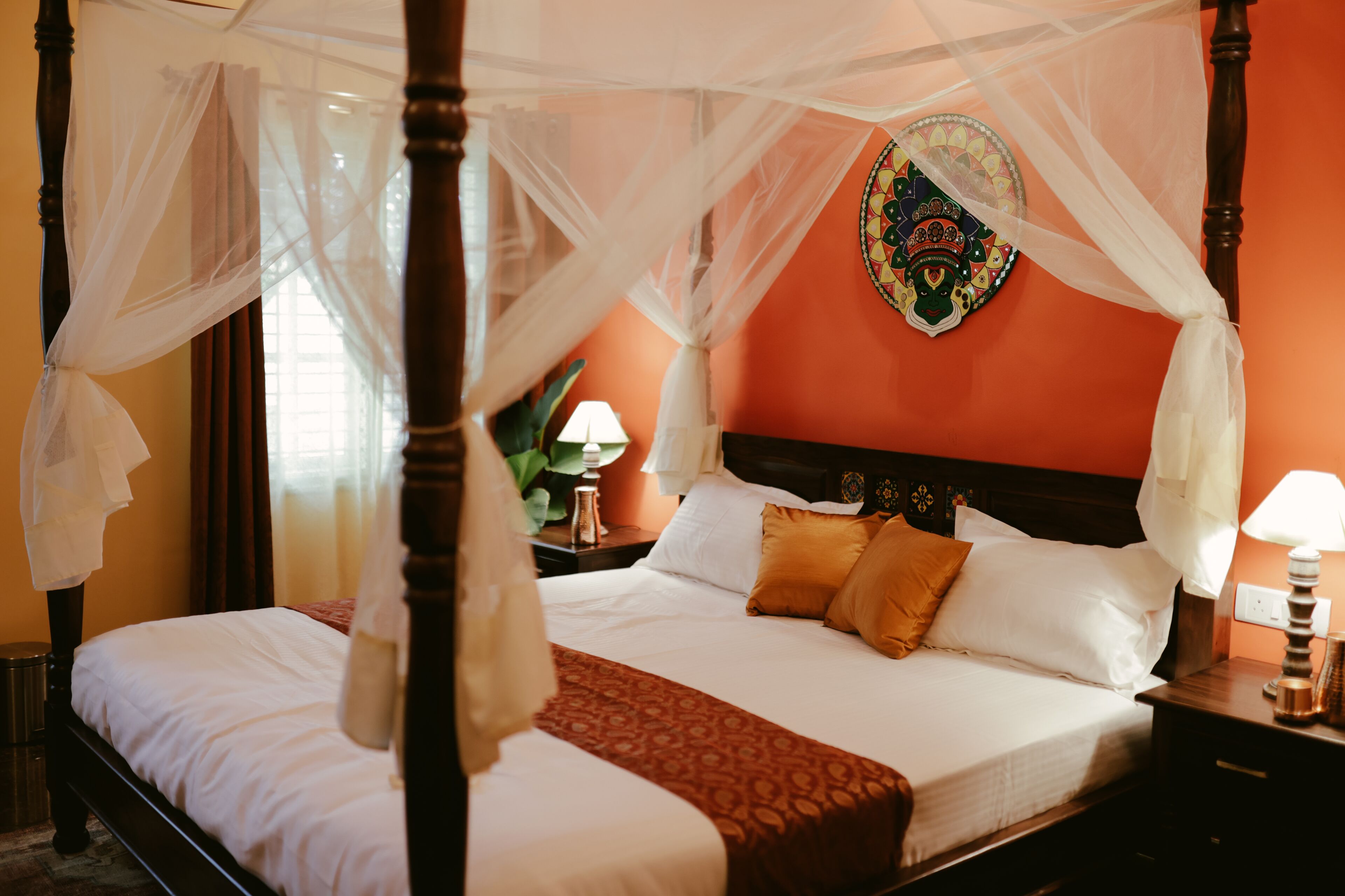 A four-poster bed with a canopy, a decorative wall hanging, and a nightstand with a lamp.