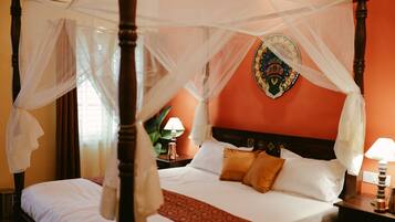 A four-poster bed with a canopy, a decorative wall hanging, and a nightstand with a lamp.