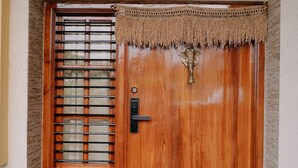 A wooden door with a metal grill, a decorative tassel, and a potted plant on either side.