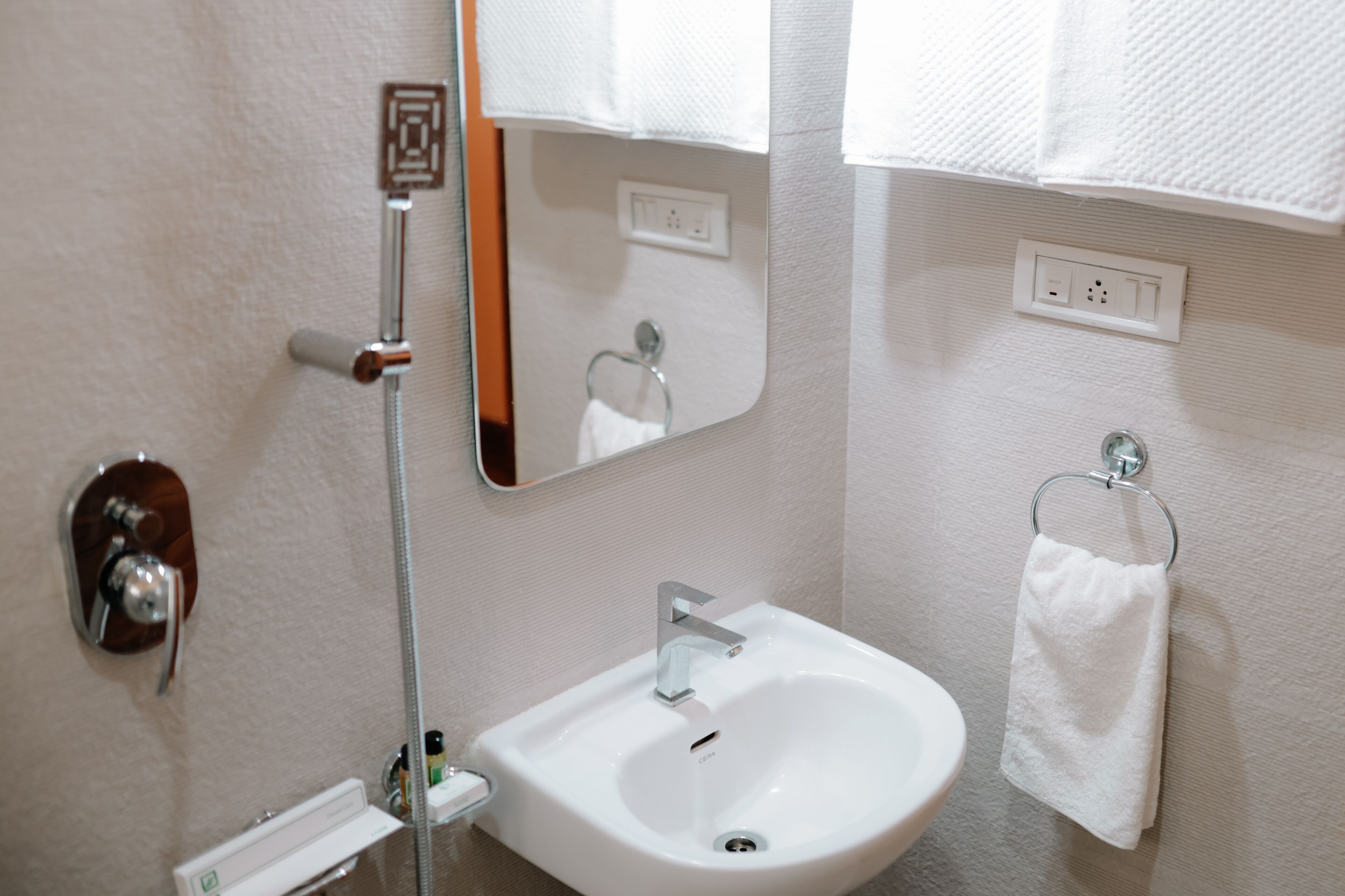 A bathroom with a white sink, a mirror, a towel rack, and a shower with a control panel.