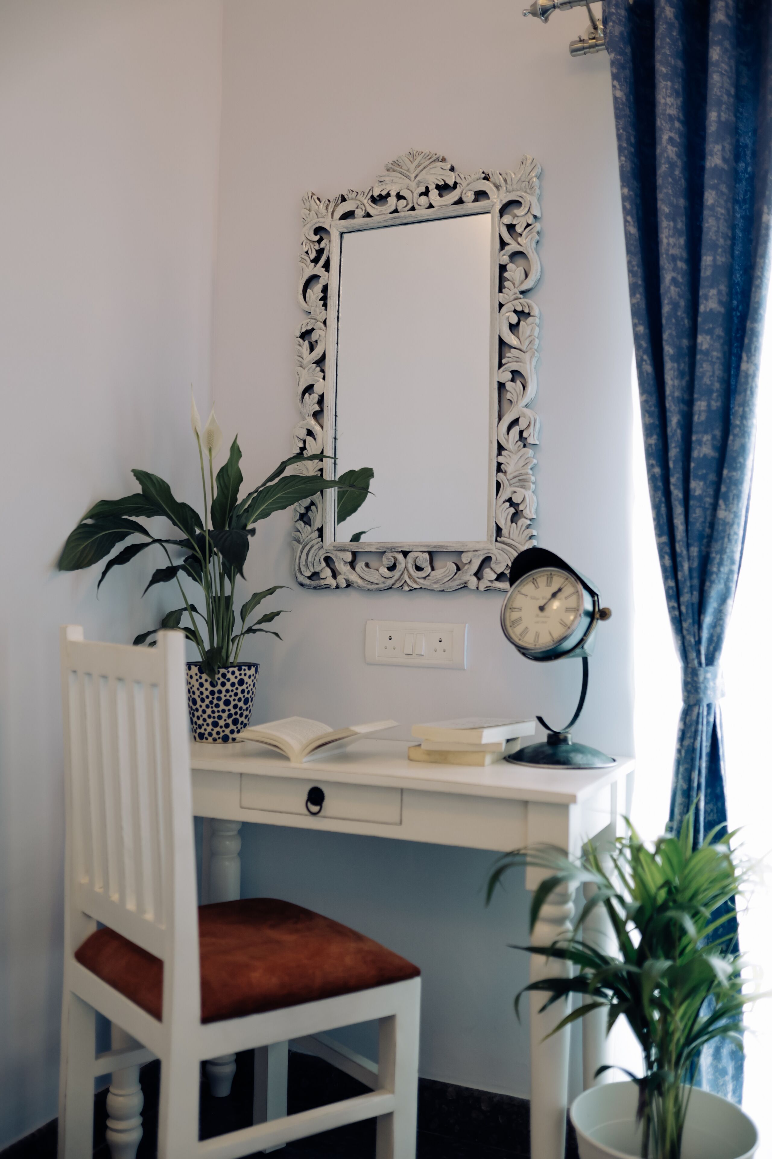 A study area with a desk, chair, books, a clock, and two potted plants.