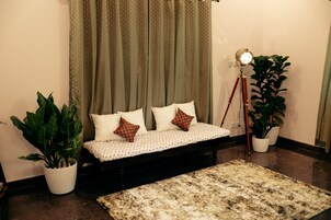 Una habitación con una cama, dos plantas en macetas, una lámpara de pie y un tapete estampado.