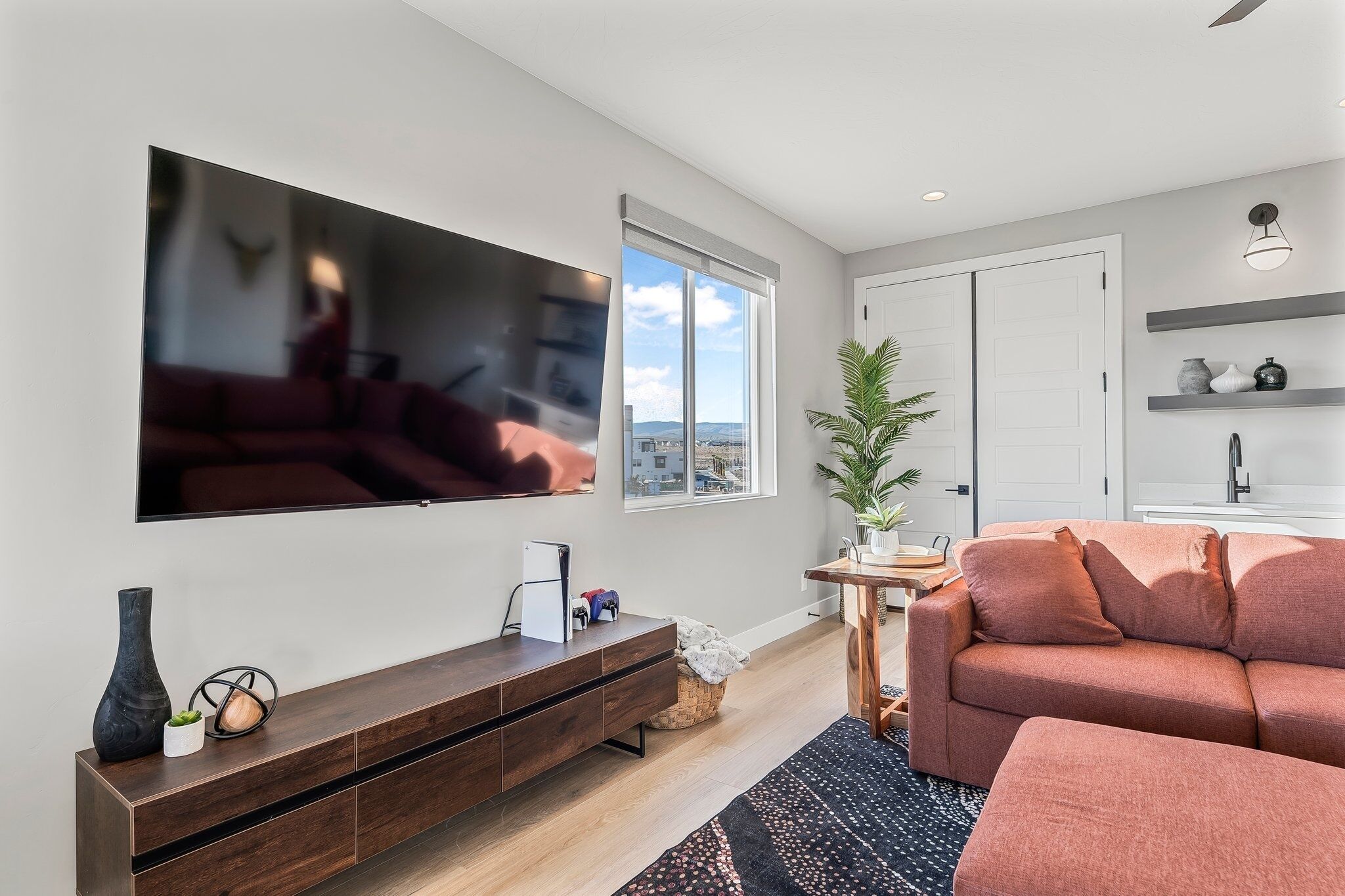 A modern living room with a flat-screen TV, a brown sofa, a wooden cabinet, and a potted plant.