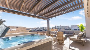 Eine Dachterrasse mit Whirlpool, Sitzgelegenheiten im Freien und Blick auf Gebäude im Hintergrund.