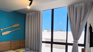 Een hotelkamer met een bed, een bureau, een stoel, een raam met gordijnen en uitzicht op de lucht.