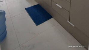 Een moderne keuken met beige kastjes, een zwart aanrecht en een ingebouwde oven. Op de vloer ligt een blauw vloerkleed en links staat een koelkast.