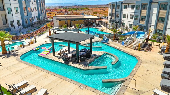 Una gran piscina al aire libre con tumbonas y una zona de estar cubierta, rodeada de edificios modernos y vistas al paisaje.