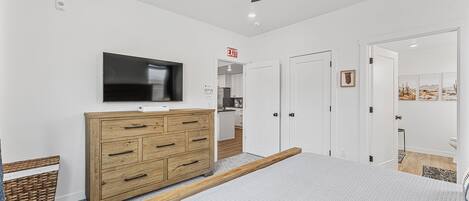 A bedroom with a bed, a wooden dresser, a television, and a ceiling fan.