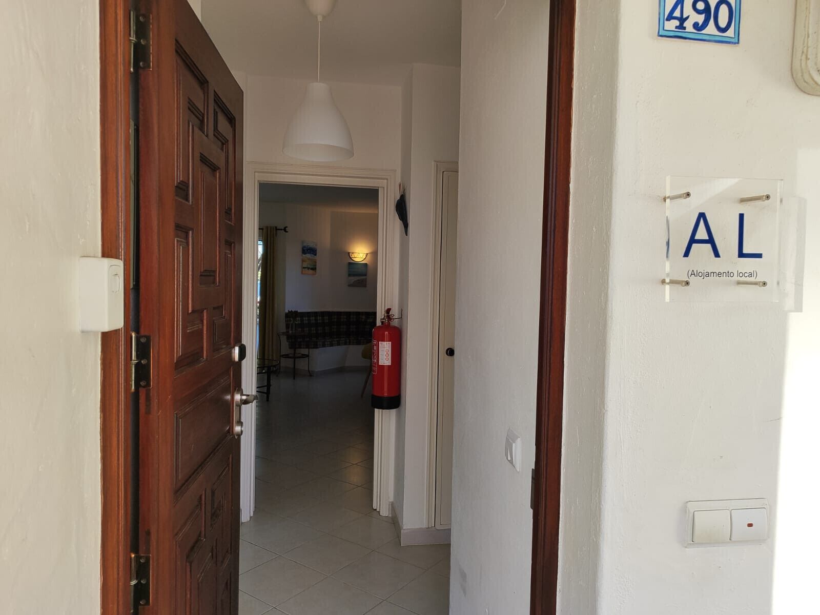 A hallway with a wooden door, a fire extinguisher, and a sign indicating room number 490.