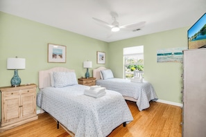 A bedroom with two beds, a ceiling fan, bedside tables with lamps, and artwork on the walls.
