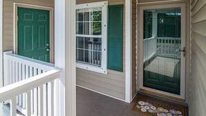 Un porche con puerta verde, una ventana con contraventanas y una puerta de cristal con un letrero con la letra 'C'.