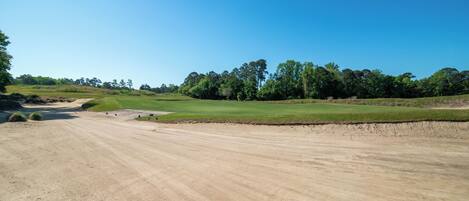 En golfbana med klar himmel, sandbunkrar och grönskande fairways.