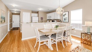 Una cocina moderna con armarios blancos, una isla central y una zona de comedor con sillas blancas.