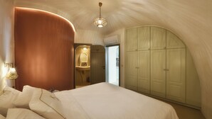 Un dormitorio con pared curva, cama con ropa blanca, lámpara colgante y armario.