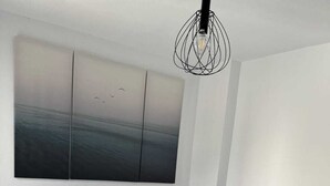 Une chambre à coucher moderne, avec un lit, une table de chevet, un tableau accroché au mur et un luminaire suspendu original.