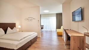 A hotel room with a bed, a desk, a chair, a TV, and a window with curtains. - Haus am See Stubenberg (Stubenberg)