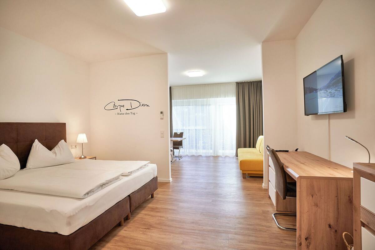 Ein Hotelzimmer mit Bett, Schreibtisch, Stuhl, Fernseher und einem fensterbepflanzten Fenster.