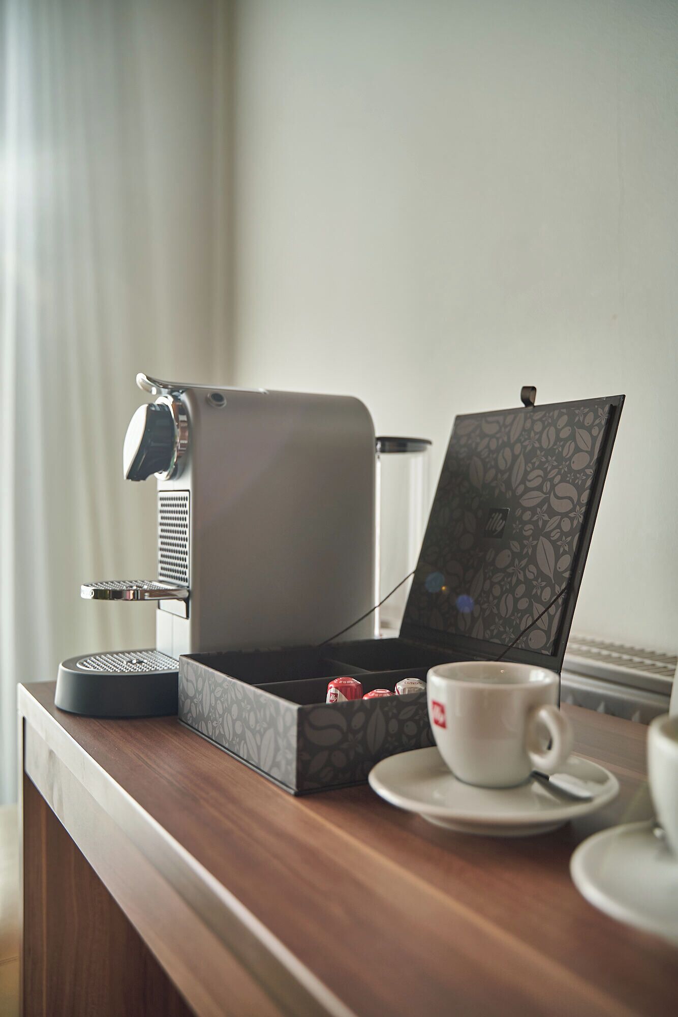 A compact espresso machine on a wooden counter with a cup of coffee and a box of tea.