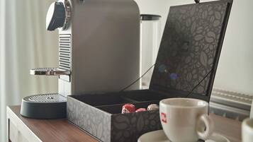A compact espresso machine on a wooden counter with a cup of coffee and a box of tea.