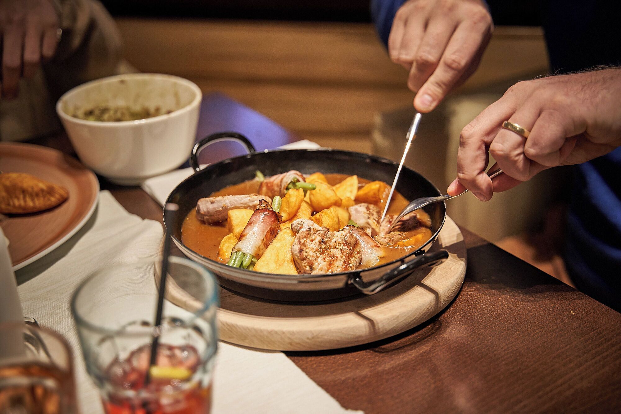 A person serving food from a pan on a wooden board.