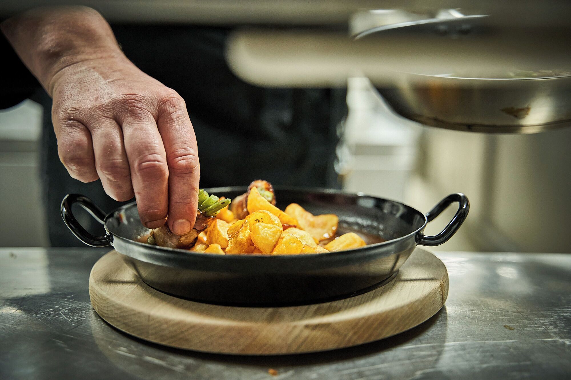 A person cooking in a kitchen with a pan on a wooden board.
