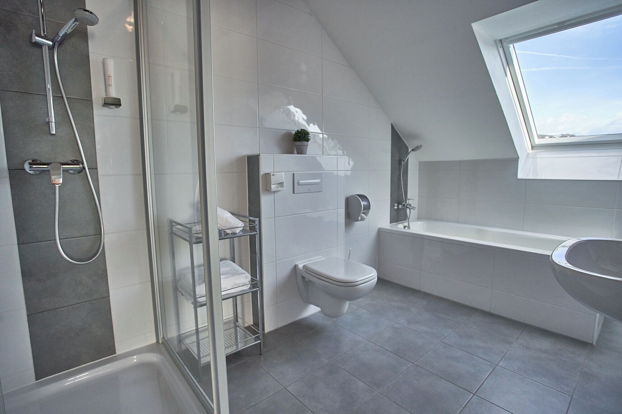 A modern bathroom with a glass-enclosed shower, a white toilet, a bathtub, and a window providing natural light.