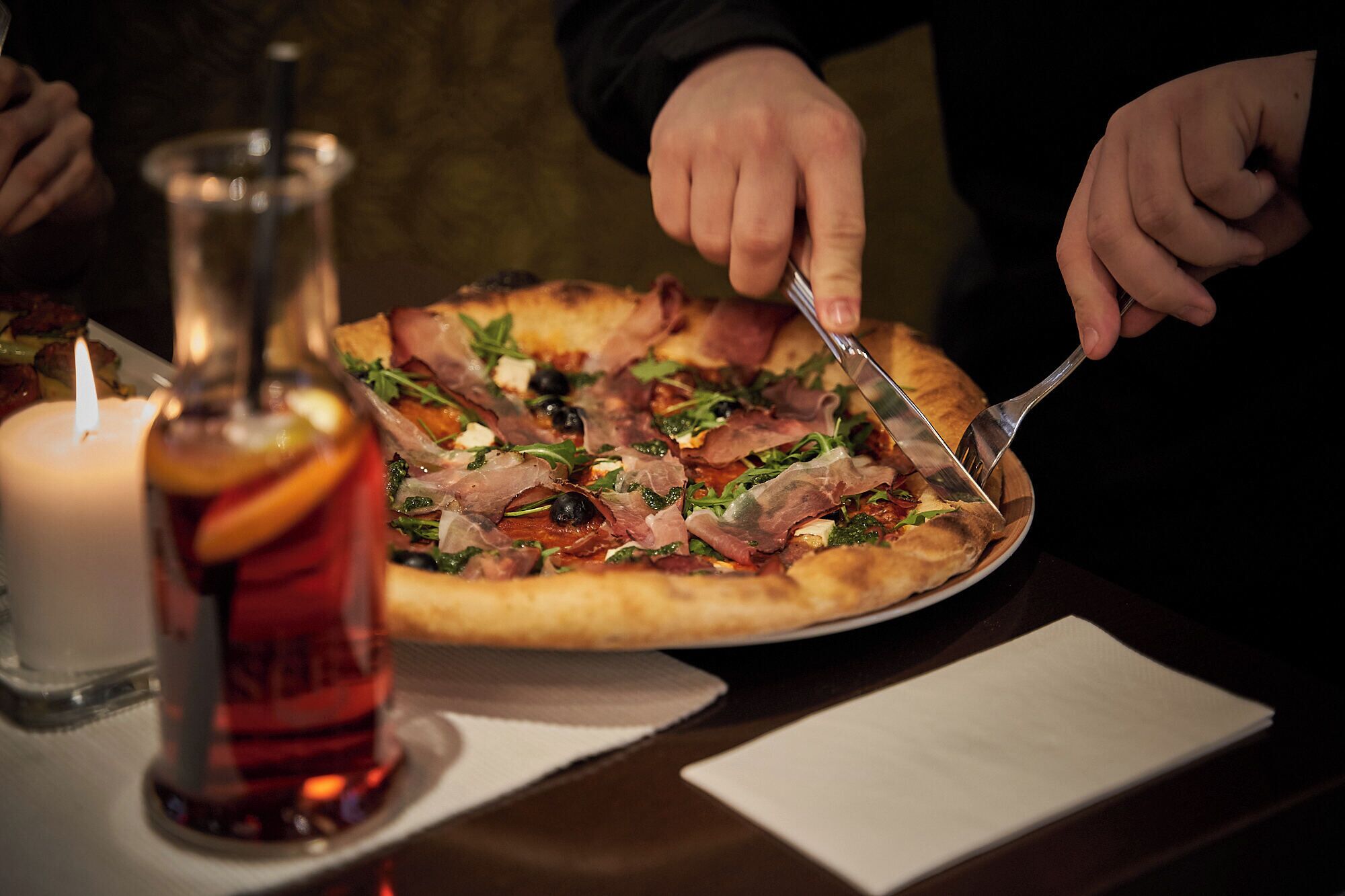Pizza com diversos ingredientes em um prato, uma vela e um frasco de molho sobre uma mesa.