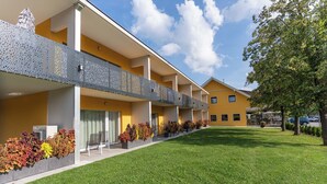 A hotel with a yellow facade, multiple balconies, and a well-maintained lawn. - Haus am See Stubenberg (Stubenberg)