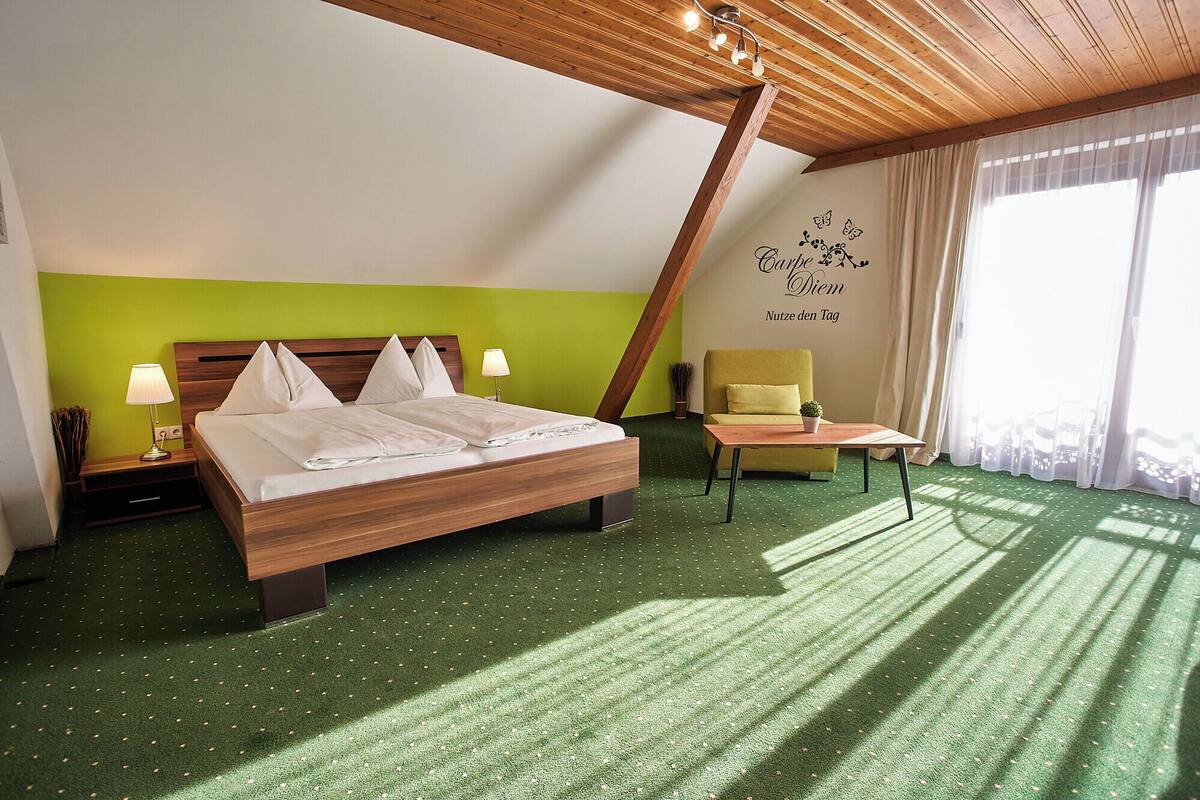 Ein Hotelzimmer mit Bett, Sessel, kleinem Tisch und einem Fenster mit Vorhängen.