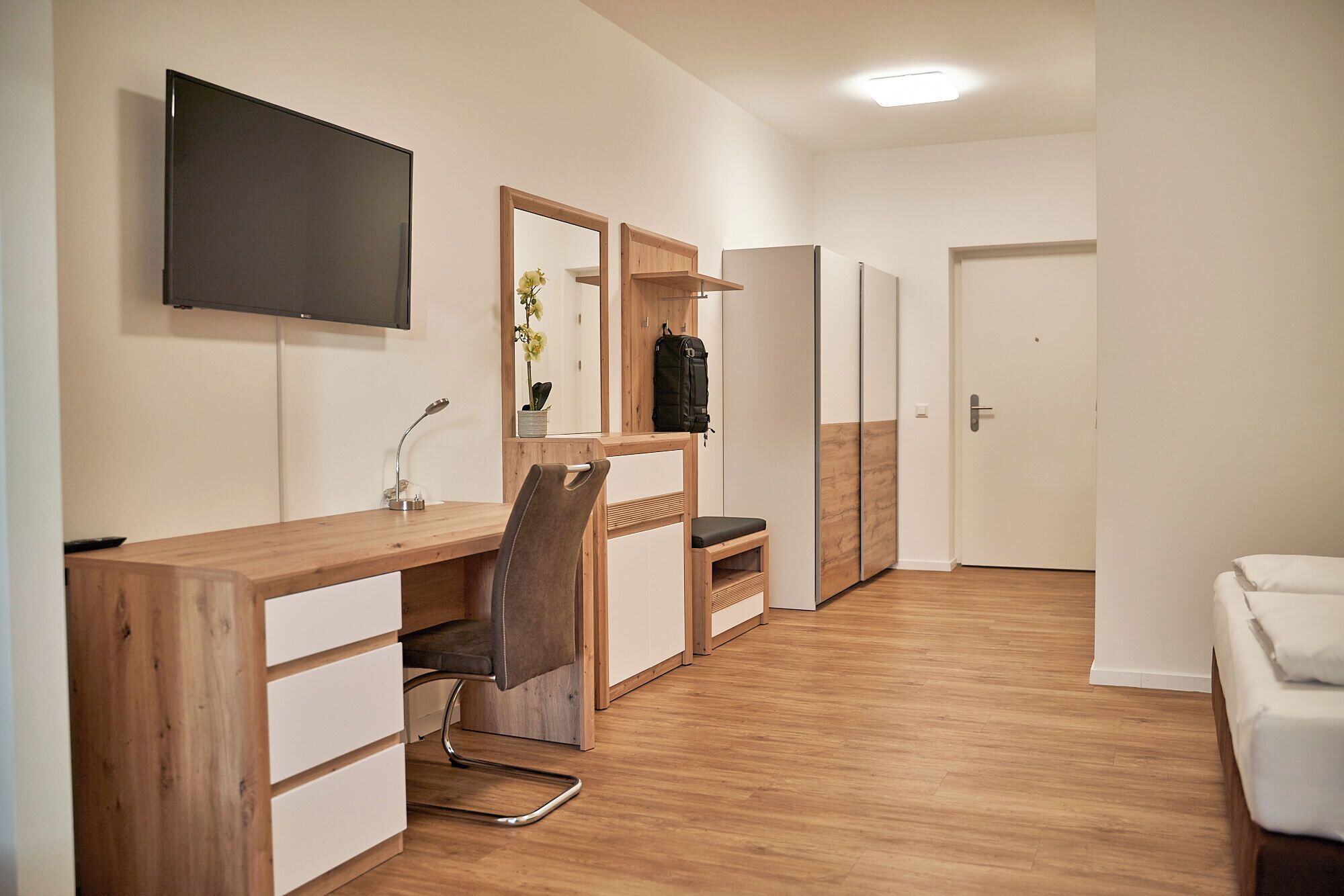 A modern room with a wooden desk, a chair, a TV, a mirror, and a wardrobe.