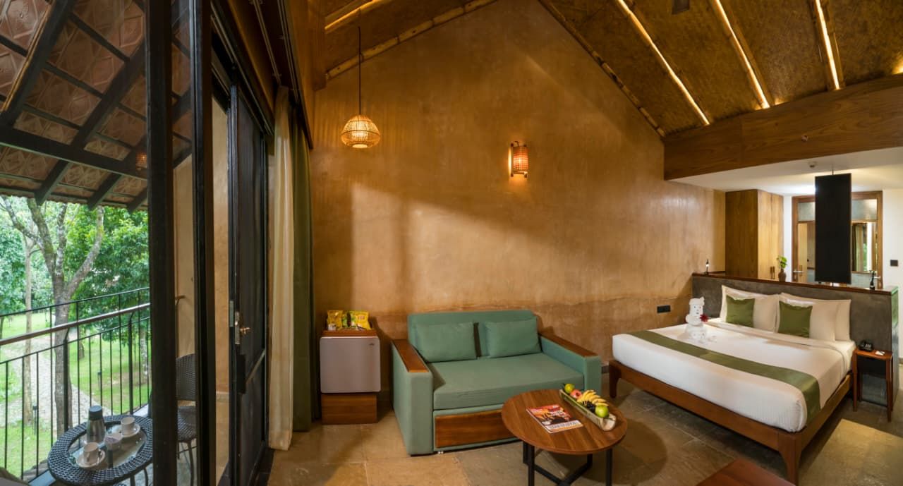 A hotel room with a bed, a sofa, a small table, and a balcony with a railing.