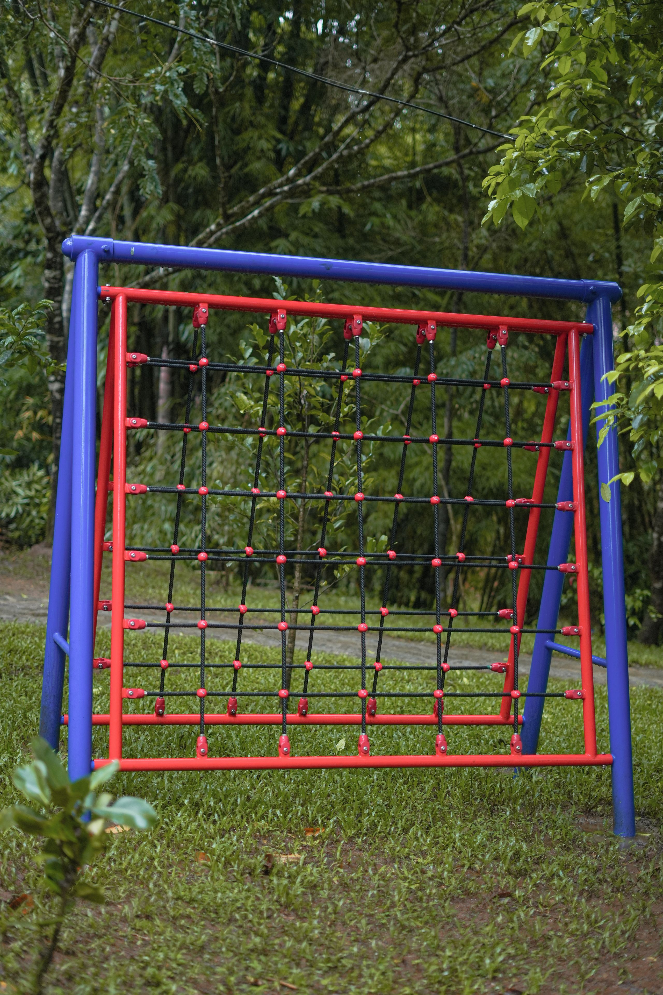 Estructura de juegos con un marco de escalada cubierto de red, rodeada de césped y árboles.
