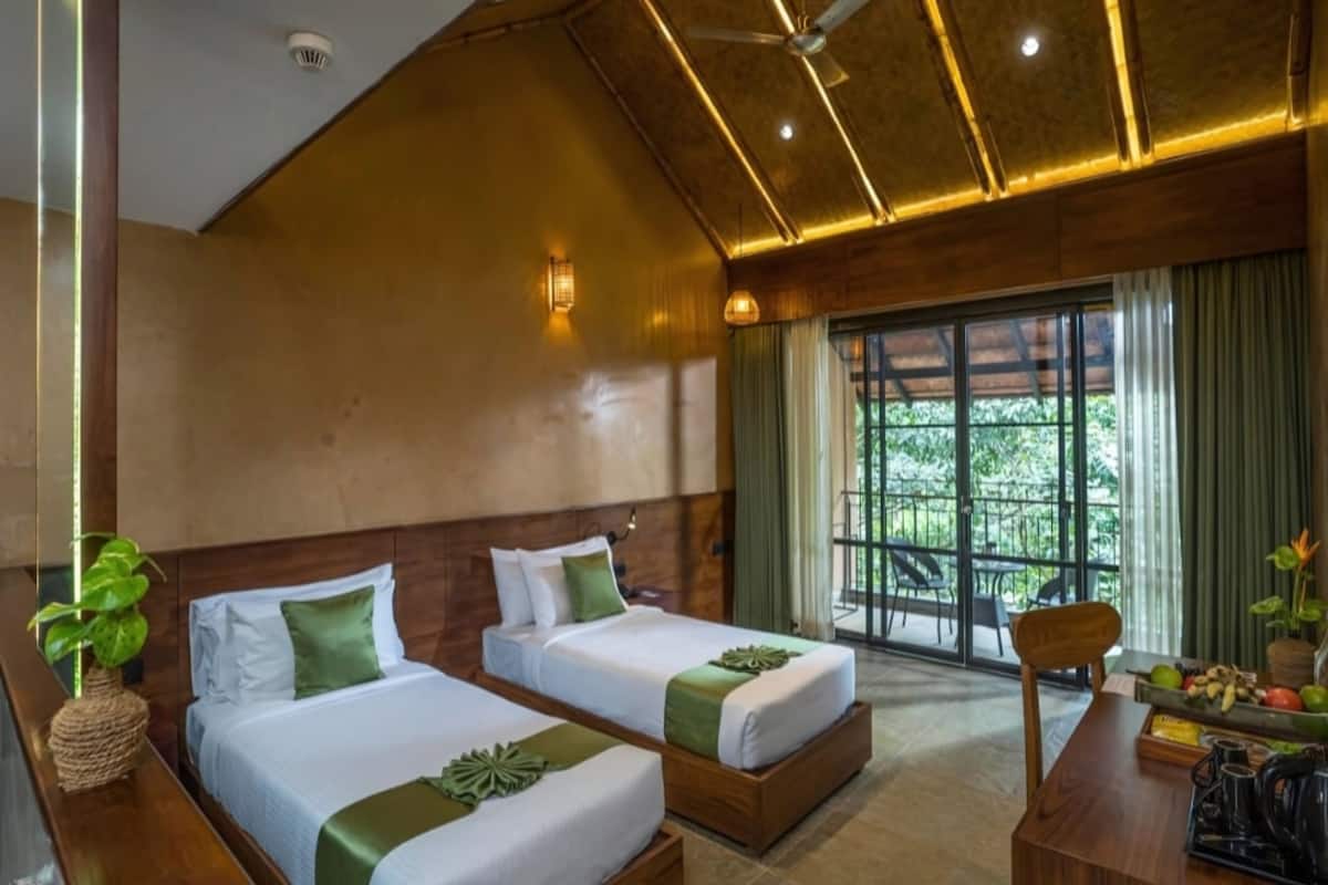 Habitación de hotel con dos camas, un escritorio de madera, una silla y vistas a la vegetación por la ventana.