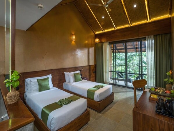 A hotel room with two beds, a wooden desk, a chair, and a view of greenery through the window.