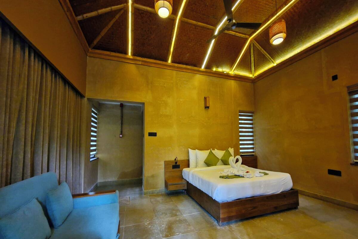 Un dormitorio amplio con una cama grande, cabecera de madera, sofá azul y techo con vigas a la vista y luminarias.