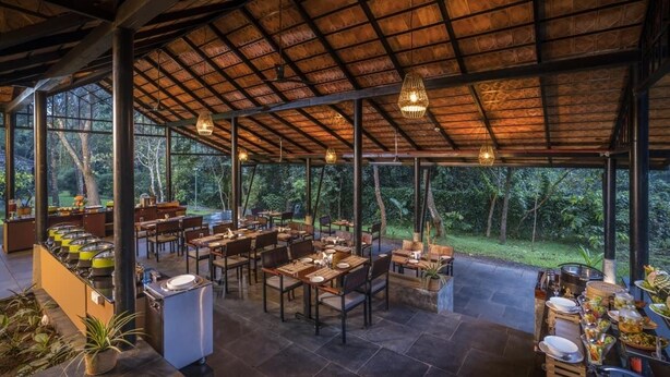 An outdoor restaurant with tables and chairs, a buffet area, and a thatched roof structure. - Klov Resort & Spa (Mananthavady)